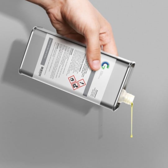 Una mano versa del liquido da un contenitore di metallo con etichetta stampata con le informazioni sul prodotto