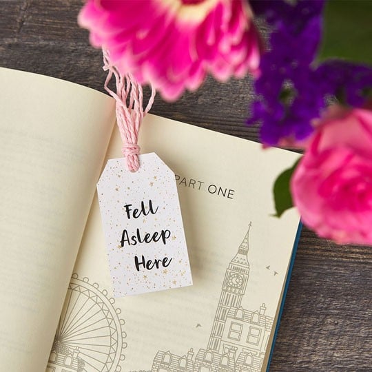 Libro aperto con cartellino stampato 'Tell Your Story' utilizzato come segnalibro e fiori rosa sullo sfondo