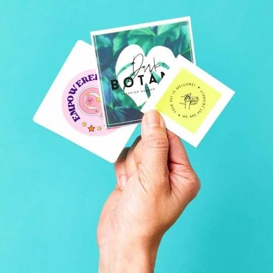 mano che tiene diversi stickers quadrati personalizzati con immagini e loghi