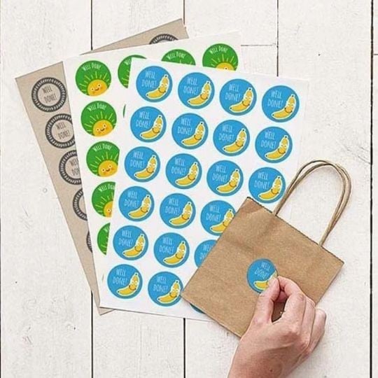 tre fogli di etichette rotonde stampate in diversi materiali accanto ad una mano che applica l'adesivo su una busta