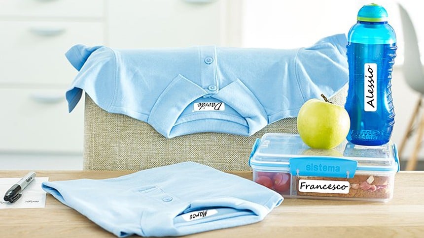 due t-shirt stese su un tavolo accanto ad una borraccia ed un porta pranzo tutti etichettati con il nome