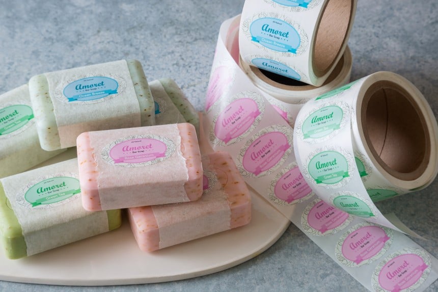 saponette con applicate delle etichette rettangolari stampate accanto ai rotoli delle stesse etichette stampate
