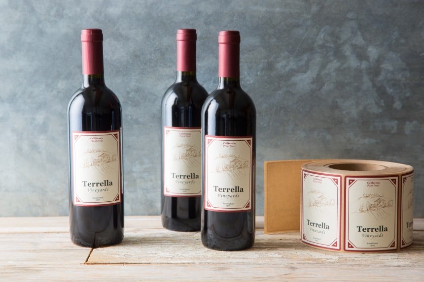 tre bottiglie di vino con applicate delle etichette rettangolari stampate accanto al rotolo di etichette