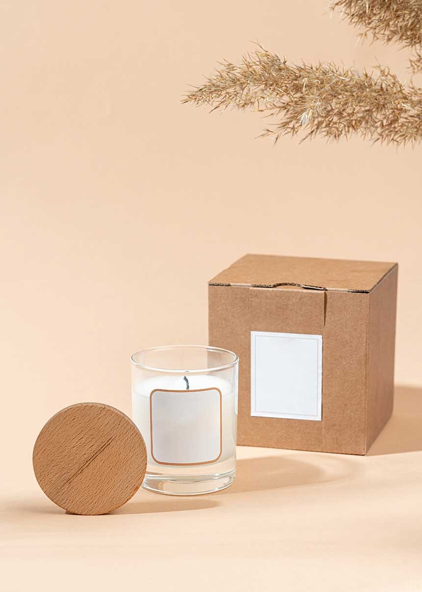 Candela con etichetta bianca e coperchio di legno, accanto a una scatola di cartone marrone con etichetta adesiva bianca