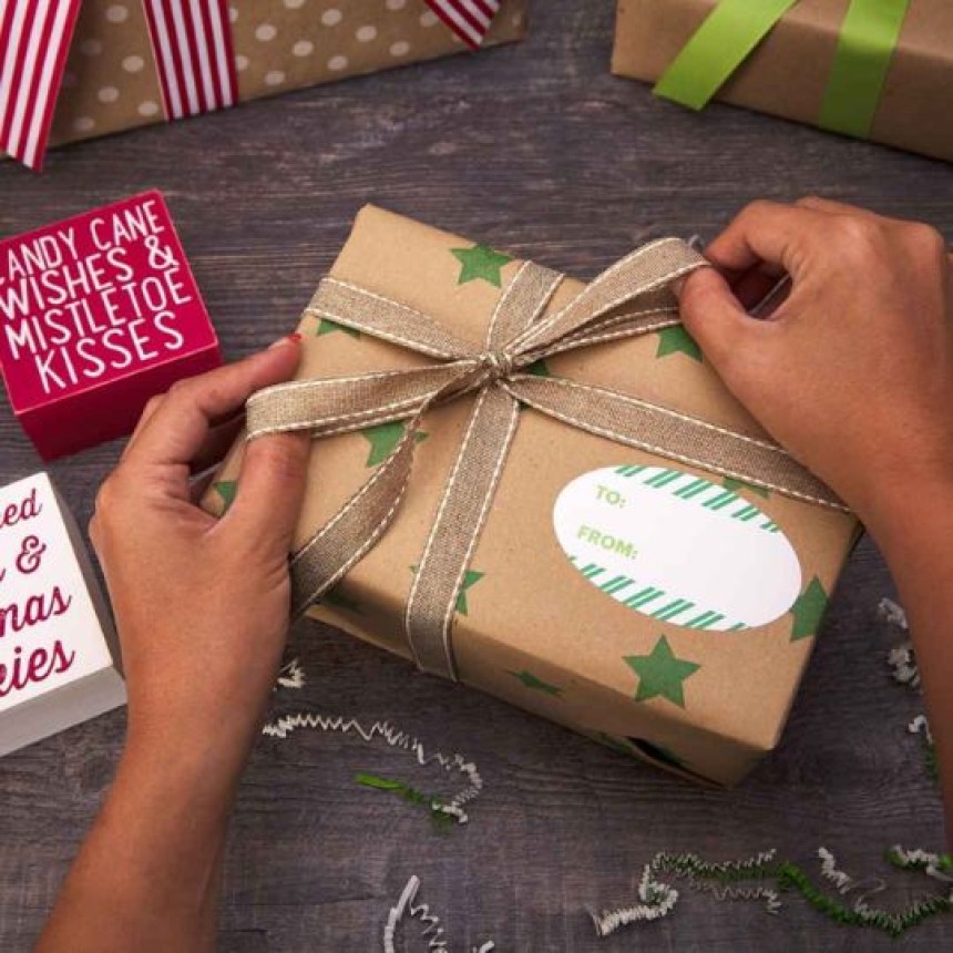Mani che chiudono un regalo con carta marrone e con un'etichetta con il nome del ricevente.