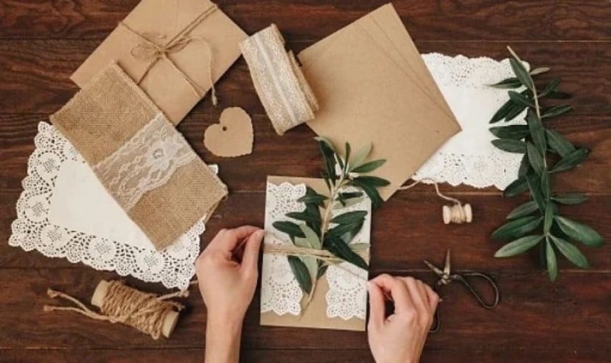 Mani che confezionano un regalo con carta marrone e decorazioni naturali su un tavolo di legno