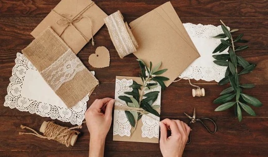 Mani che confezionano un regalo con carta marrone e decorazioni naturali su un tavolo di legno
