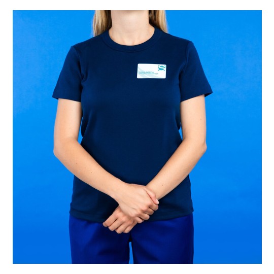 L'immagine rappresenta una persona in abbigliamento uniforme scuro, che sta in piedi con le mani incrociate, di fronte a uno sfondo blu.