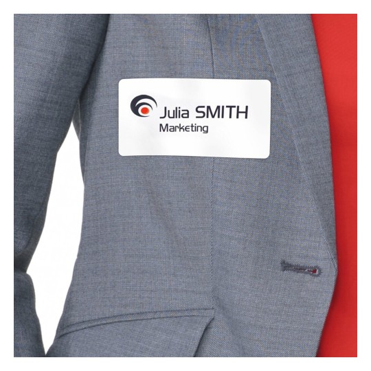 L'immagine mostra un distintivo di nome attaccato a una giacca grigia. Il distintivo riporta il nome 'Julia SMITH' e la parola 'Marketing'.