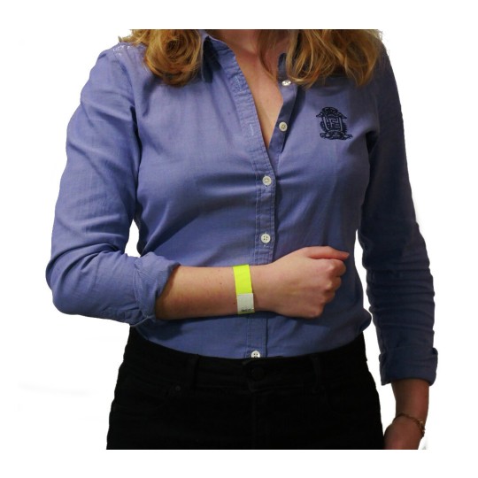 L'immagine mostra una donna con i capelli ricci, che indossa una camicia blu e ha un braccialetto giallo al polso. Sta tenendo il braccio con le mani incrociate.