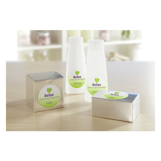 L'immagine mostra diversi prodotti per il benessere e la spa. Ci sono due bottiglie bianche di sapone per le mani e crema per le mani, oltre a due confezioni di sapone e una candela con il marchio 'Relax'.