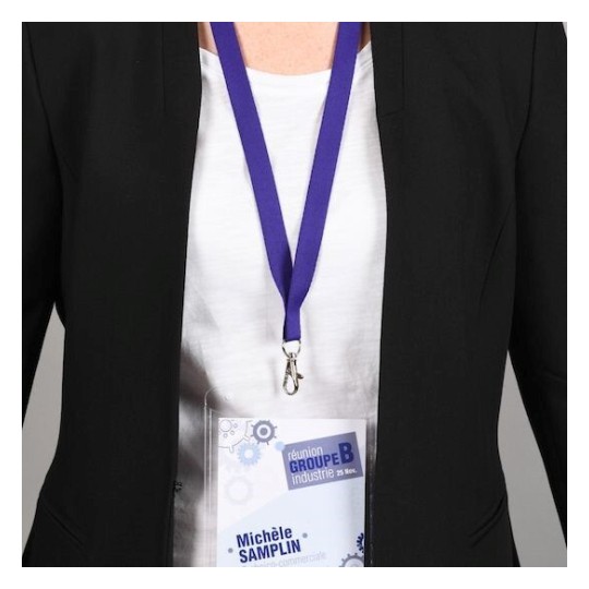 In the image, a person is wearing a black blazer over a white shirt, with a lanyard holding a name tag that features the French words for an industrial meeting and a name.