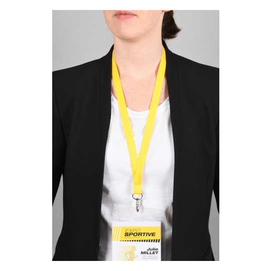Immagine di una persona che indossa un blazer nero con una maglietta bianca. Ha un distintivo appeso con un laccio giallo al collo, visibile nella parte anteriore. Il distintivo riporta il nome 'Julie Millet' e il termine 'Expo Sportive'.