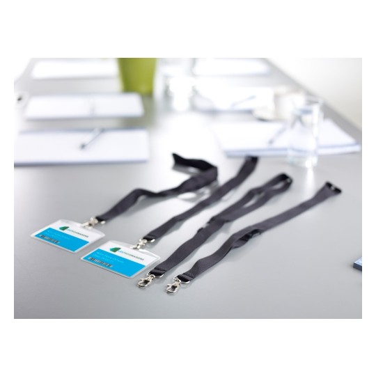 In this image, there are several ID badges attached to black lanyards placed on a table. The background includes notebooks and water glasses, indicating a meeting or conference setting.