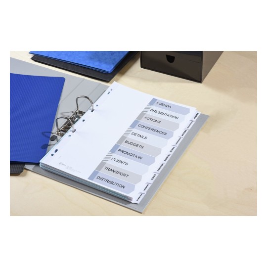 The image displays a binder organized with labeled tabs including Agenda, Presentation, Actions, Conferences, Details, Budgets, Promotion, Clients, Transport, and Distribution. It sits on a desk with a blue folder and a black storage box in the background.