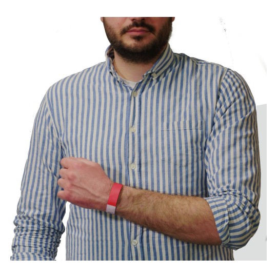 L'immagine mostra un uomo con una camicia a righe blu e bianche che tiene un braccio con un braccialetto rosso. Il braccialetto sembra essere di tipo identificativo, comune in eventi o servizi.