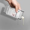 Una mano versa del liquido da un contenitore di metallo con etichetta stampata con le informazioni sul prodotto