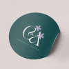 adesivo rotondo verde con logo stilizzato con iniziali e un fiore bianco.