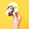 mano che tiene diversi sticker rotondi personalizzati stampati con loghi e immagini