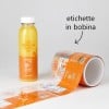 Bottiglia di succo d'arancia con etichetta adesiva arancione e rotolo di etichette stampate con lo stesso testo