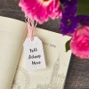 Libro aperto con cartellino stampato 'Tell Your Story' utilizzato come segnalibro e fiori rosa sullo sfondo