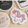Adesivo di un unicorno sorridente con criniera arcobaleno e corno dorato, circondato da altri adesivi stampati