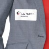 L'immagine mostra un distintivo di nome attaccato a una giacca grigia. Il distintivo riporta il nome 'Julia SMITH' e la parola 'Marketing'.