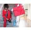 Immagine di una bambina che si allaccia le scarpe, indossando un maglione rosso e collant rossi, con una borsa rossa accanto a lei. C'è anche un personaggio animato blu che saluta.