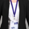 In the image, a person is wearing a black blazer over a white shirt, with a lanyard holding a name tag that features the French words for an industrial meeting and a name.