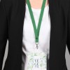 Un badge suspendu à un cordon vert, porté par une personne en veste noire et t-shirt clair, avec des motifs végétaux sur le badge.