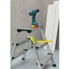Ladder with a cordless drill and measuring tape on it, against a neutral background.
