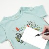 L'immagine mostra una maglietta azzurra per bambini con un design stampato. Accanto, una persona sta scrivendo su un'etichetta bianca con un pennarello.