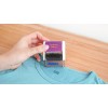 In the image, a hand is holding a clothing stamp labeled 'Clothing Stamp' from the brand Avery, positioned over the collar of a light blue t-shirt on a wooden surface.