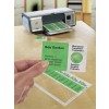 The image shows a printer on a table with printed green business cards and labels. A hand is holding one card that features contact information alongside a globe icon and multiple language translations.